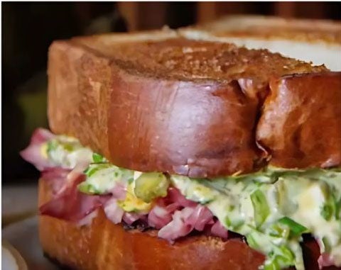 Thick-cut toasted sandwich with tender meat and a creamy herb filling on a rustic plate.