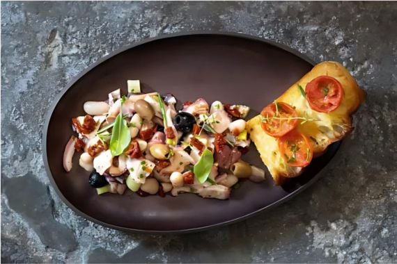 Octopus and bean salad with sun-dried tomatoes and olives, served with toasted bread topped with cherry tomatoes.