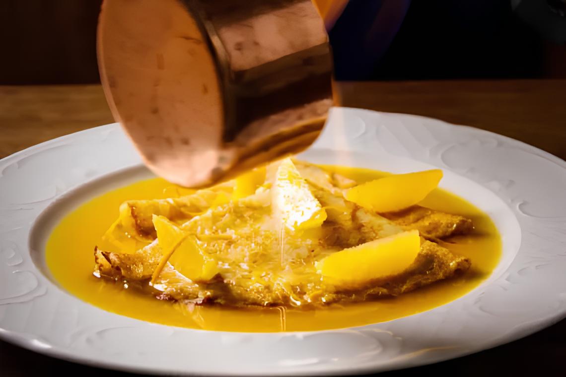 Crepes drenched in orange sauce with peach slices, served on a white plate for a delightful dessert experience.
