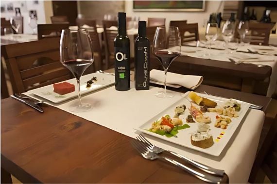 A rustic table setting featuring Croatian olive oils, red wine, and a variety of appetizers on elegant white plates.