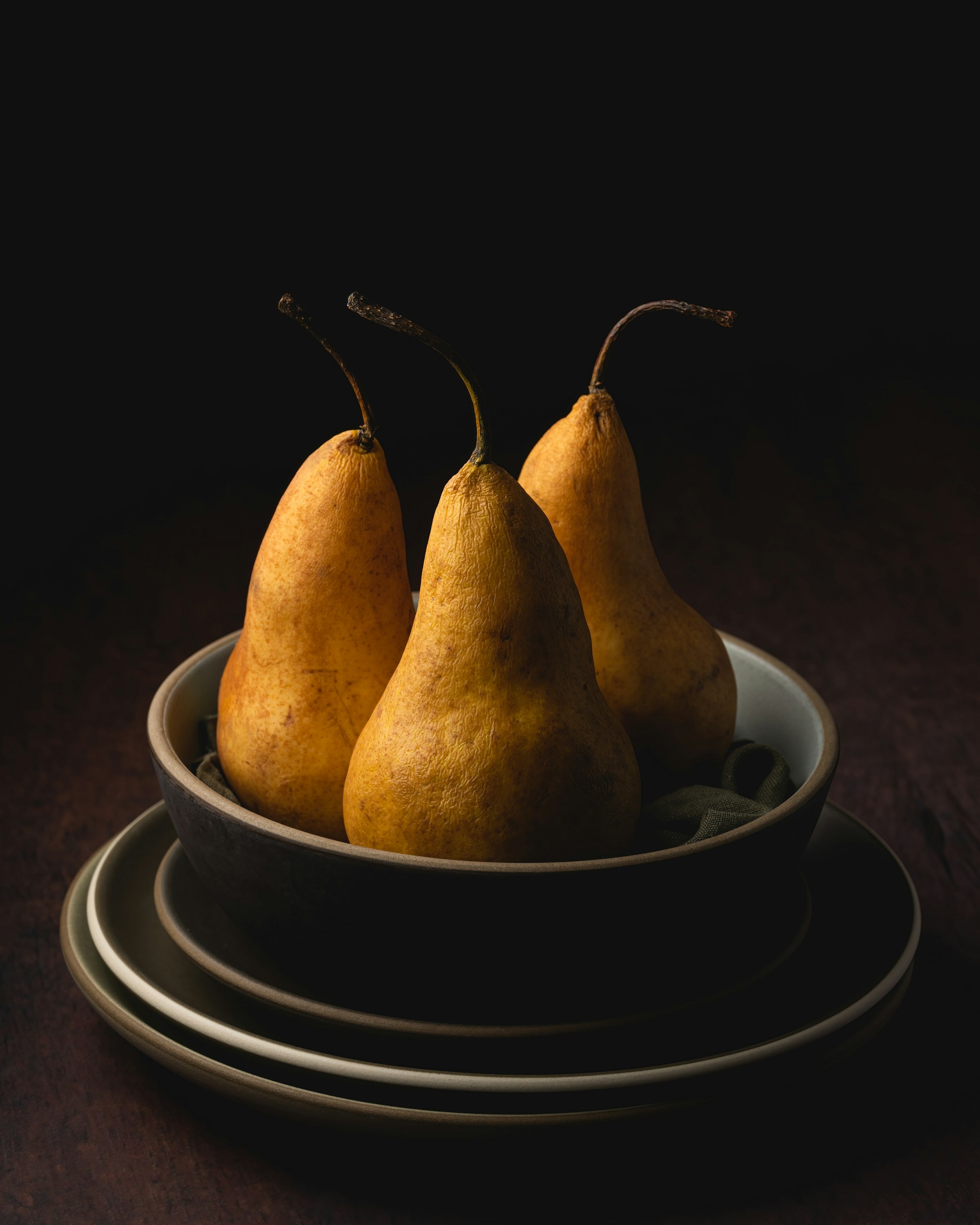 A trio of pears set in in a bowl on a stack of ceramic plates