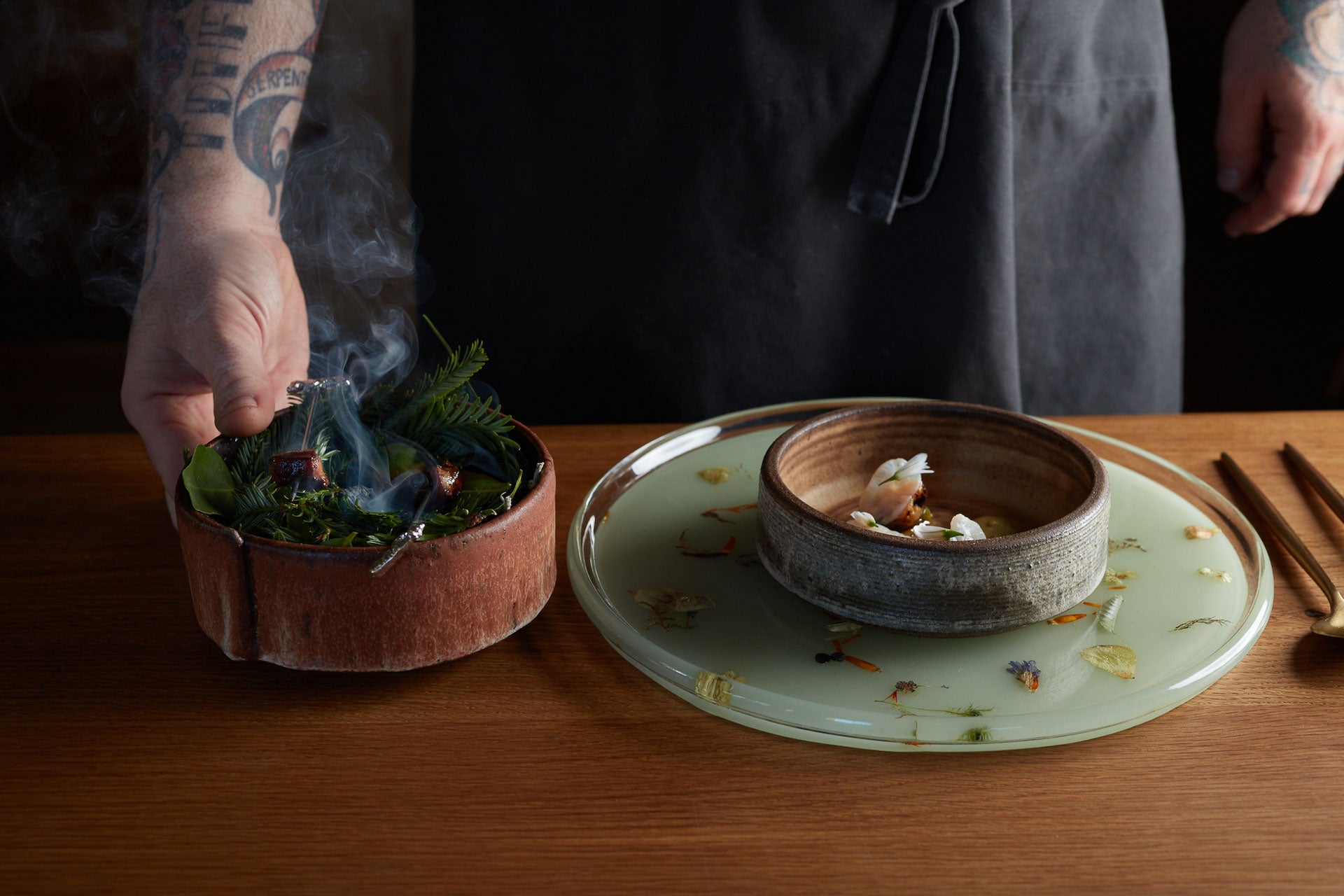 Two fine dining dishes, one filled with cooked green leaves.