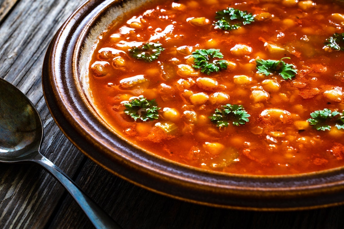 A vibrant bowl of harira soup set down on a table next to a spoon