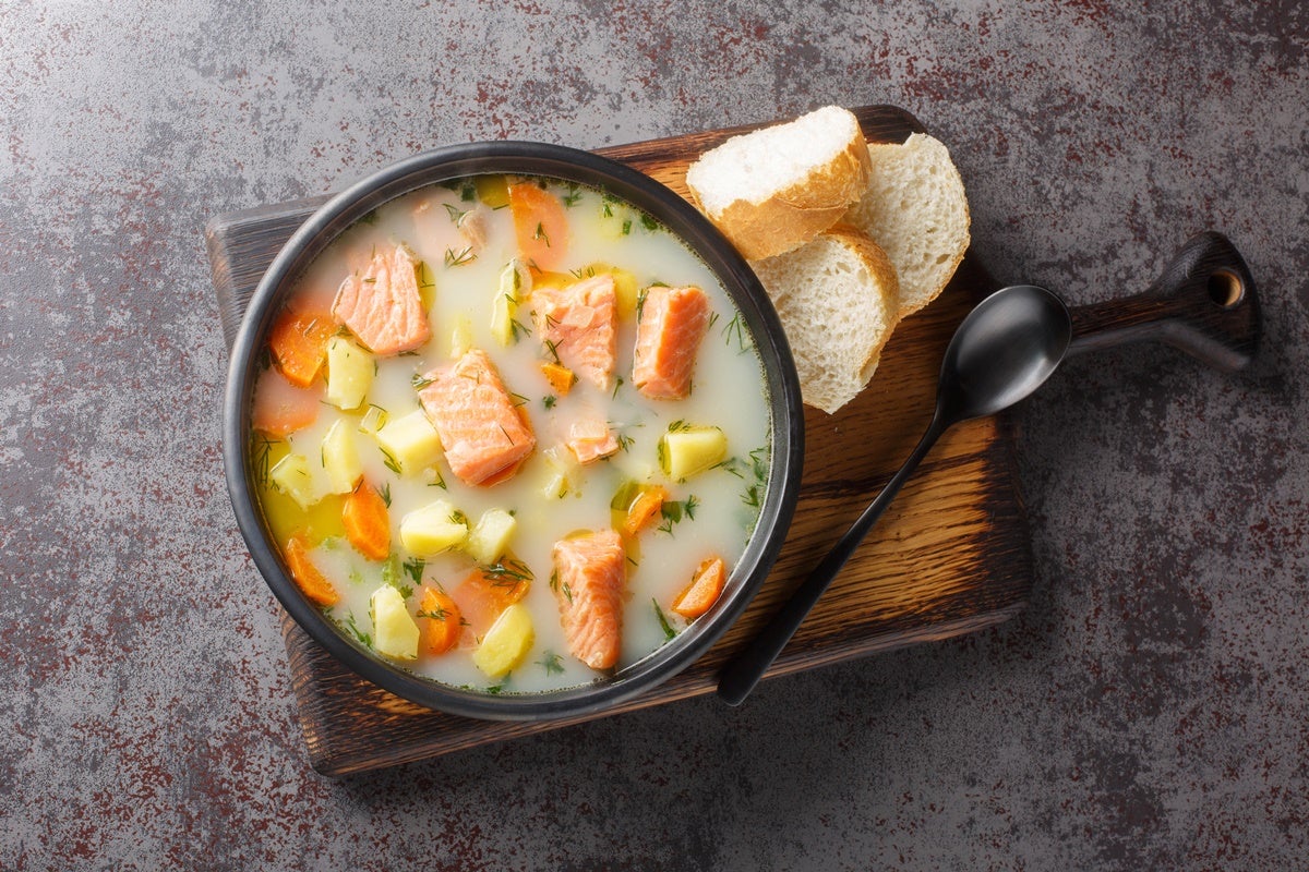 A bowl of creamy salmon laden lohiketto soup set on a board with slices of bread