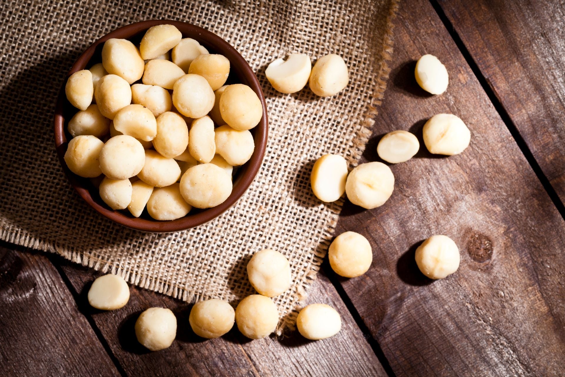 An overhead photo of a bowl of shelled macademia nuts spilling out