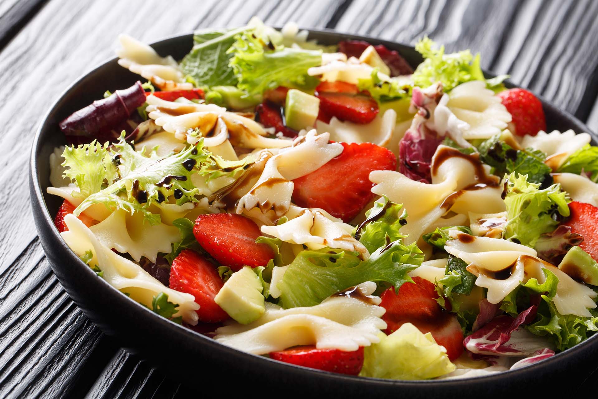 Refreshing pasta salad farfalle with avocado, strawberries, lettuce and balsamic sauce close-up on a plate on the table