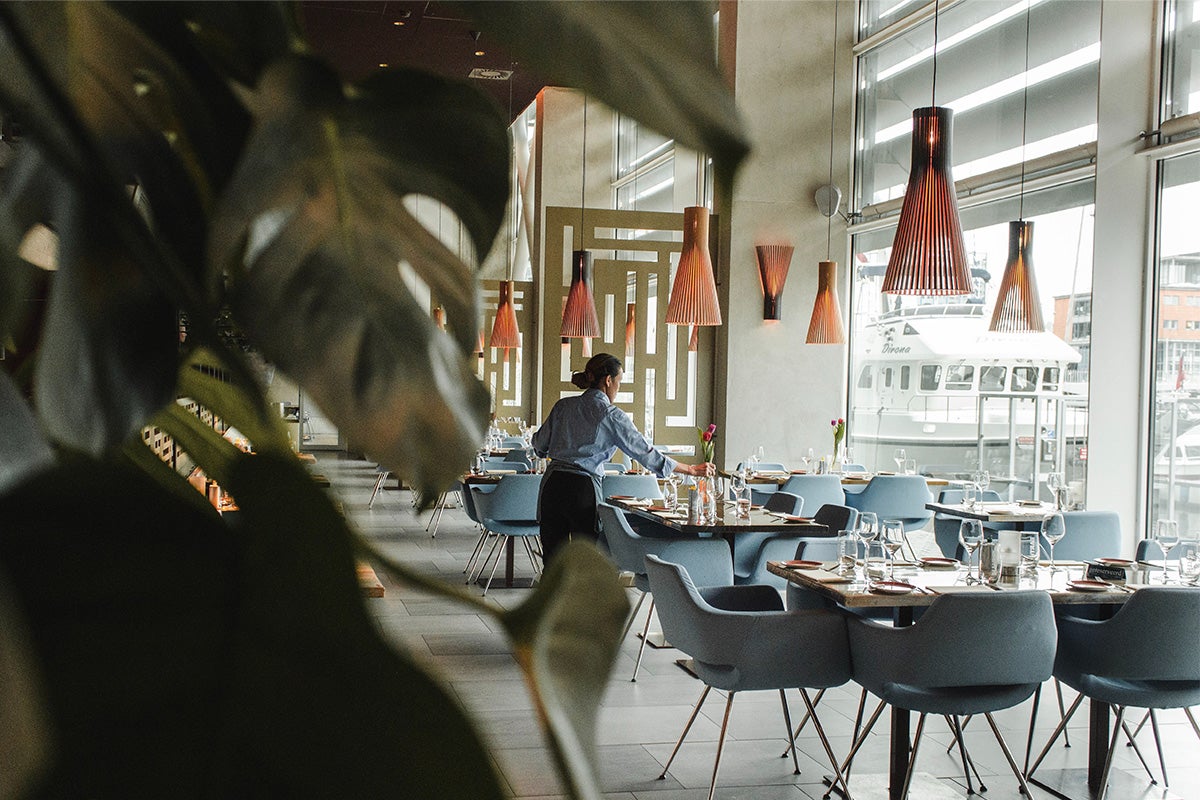 A woman laying tables in a light-filled restaurant dining room.