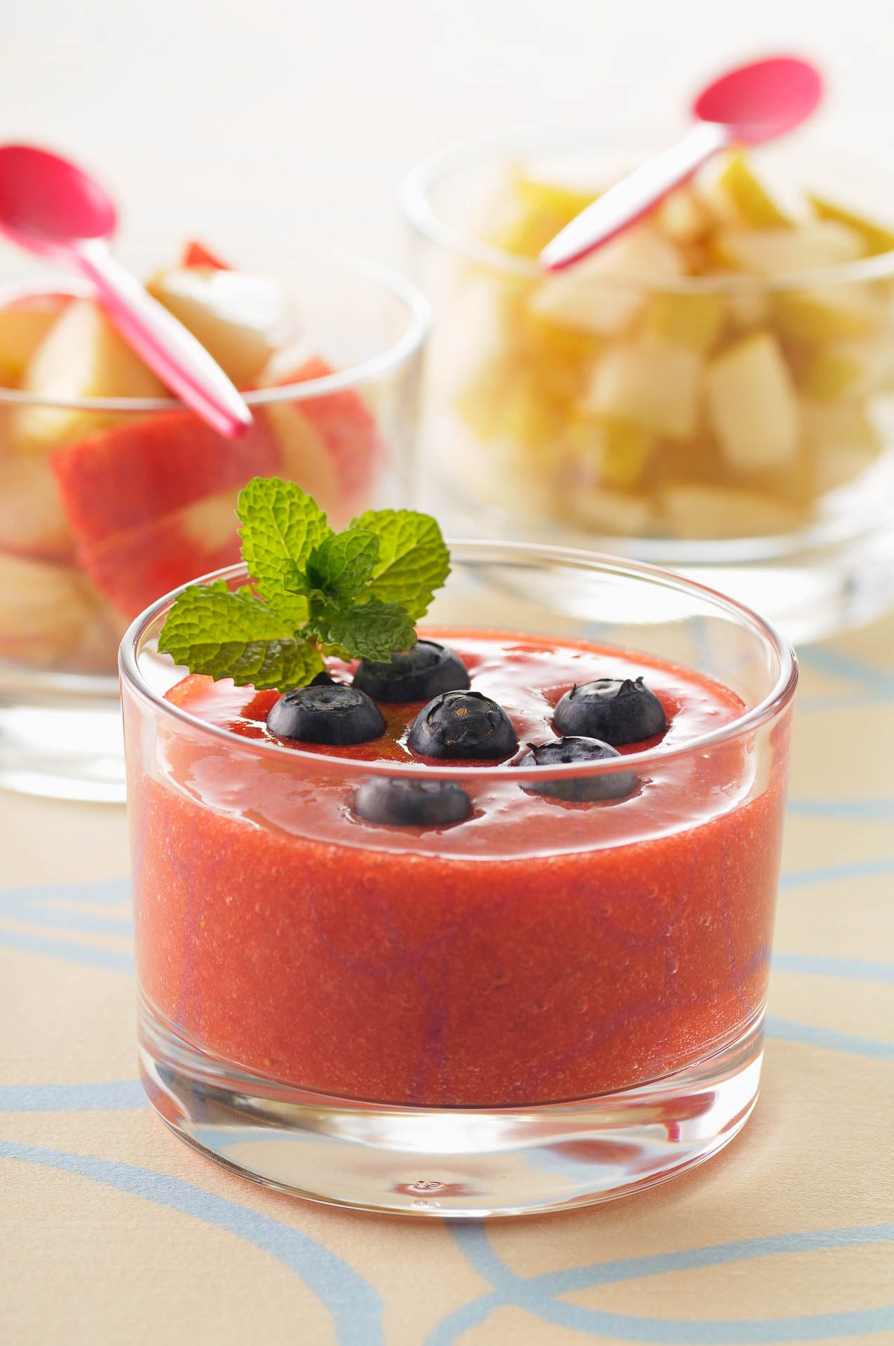 a glass of strawberry gazpacho topped with a sprig of mint and blueberries
