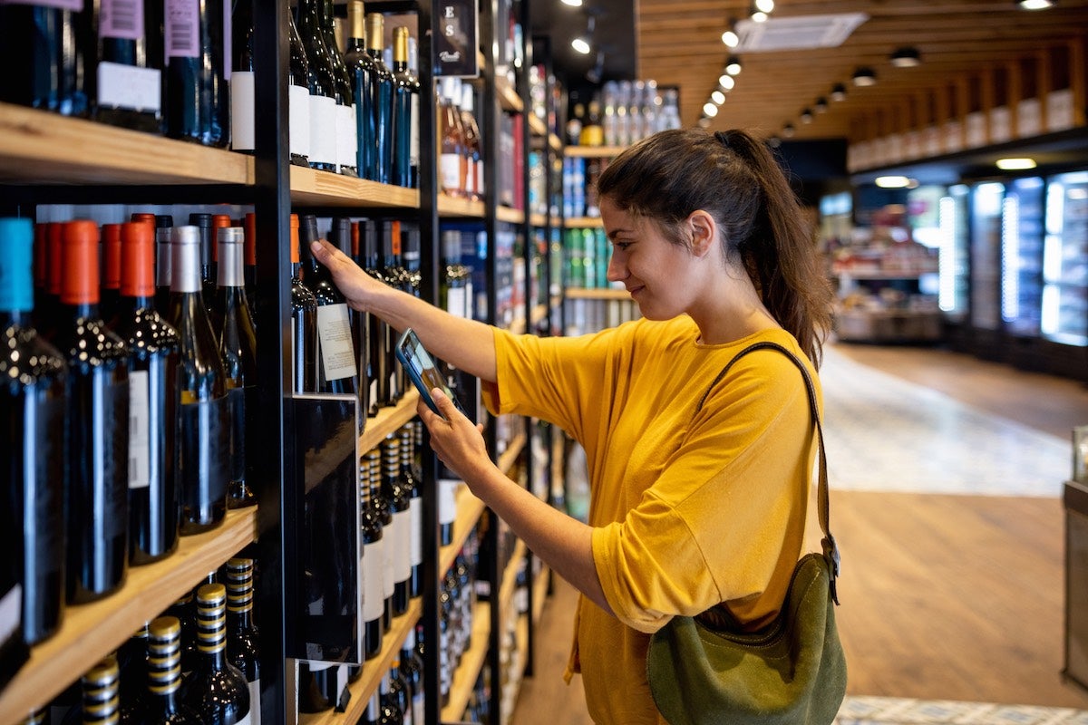 Girl using wine app on smartphone before buying a wine bottle