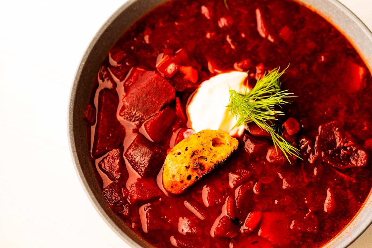 A brightly colored bowl of vibrant red borscht soup topped with garnish and cream