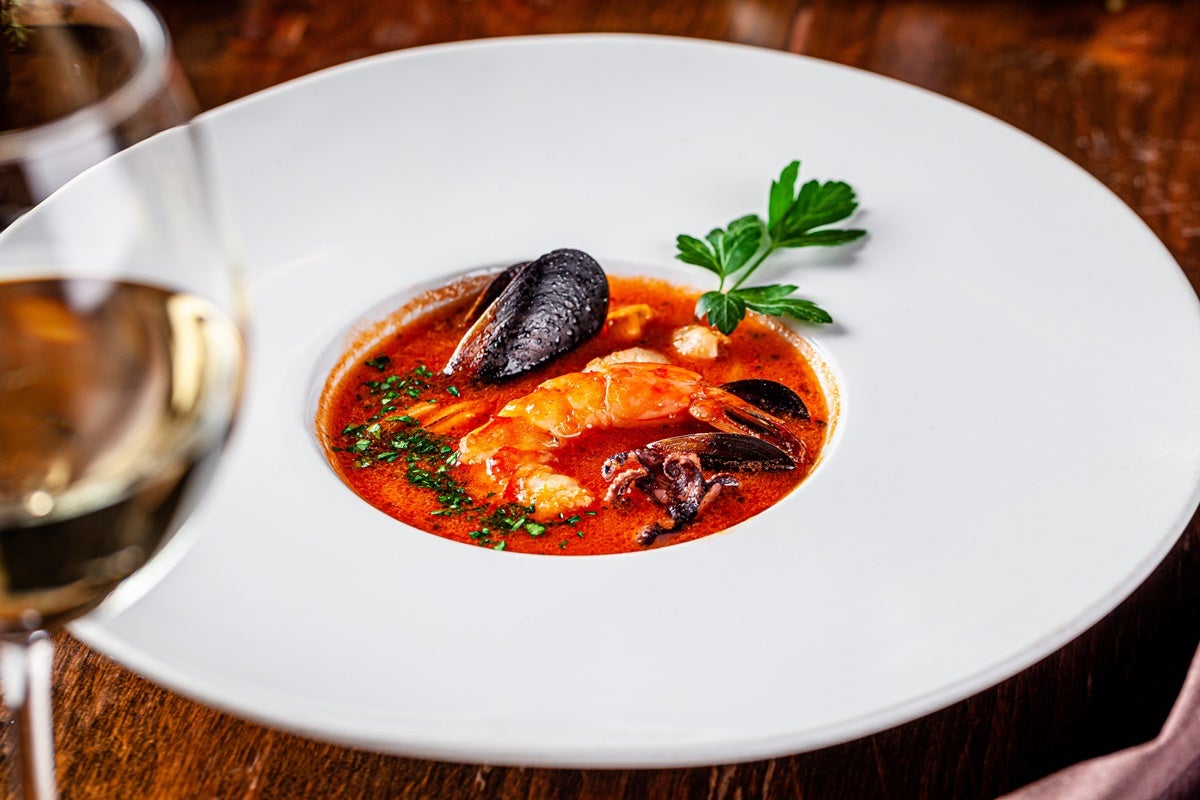 An elegant bowl filled with a rich bouillabaisse soup with seafood, set next to a glass of white wine