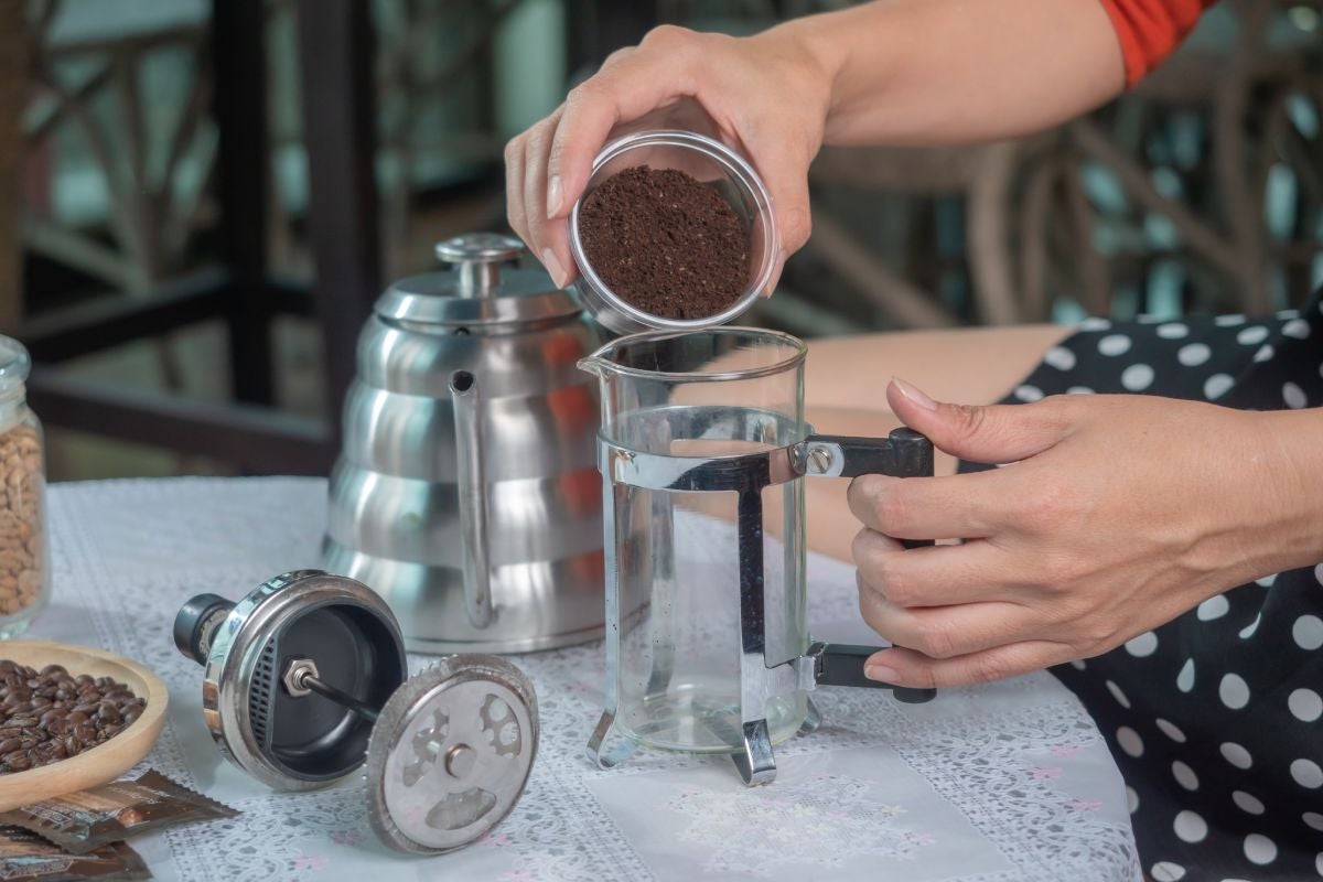Woman pouring coffee powder in a french press to brew hot coffee