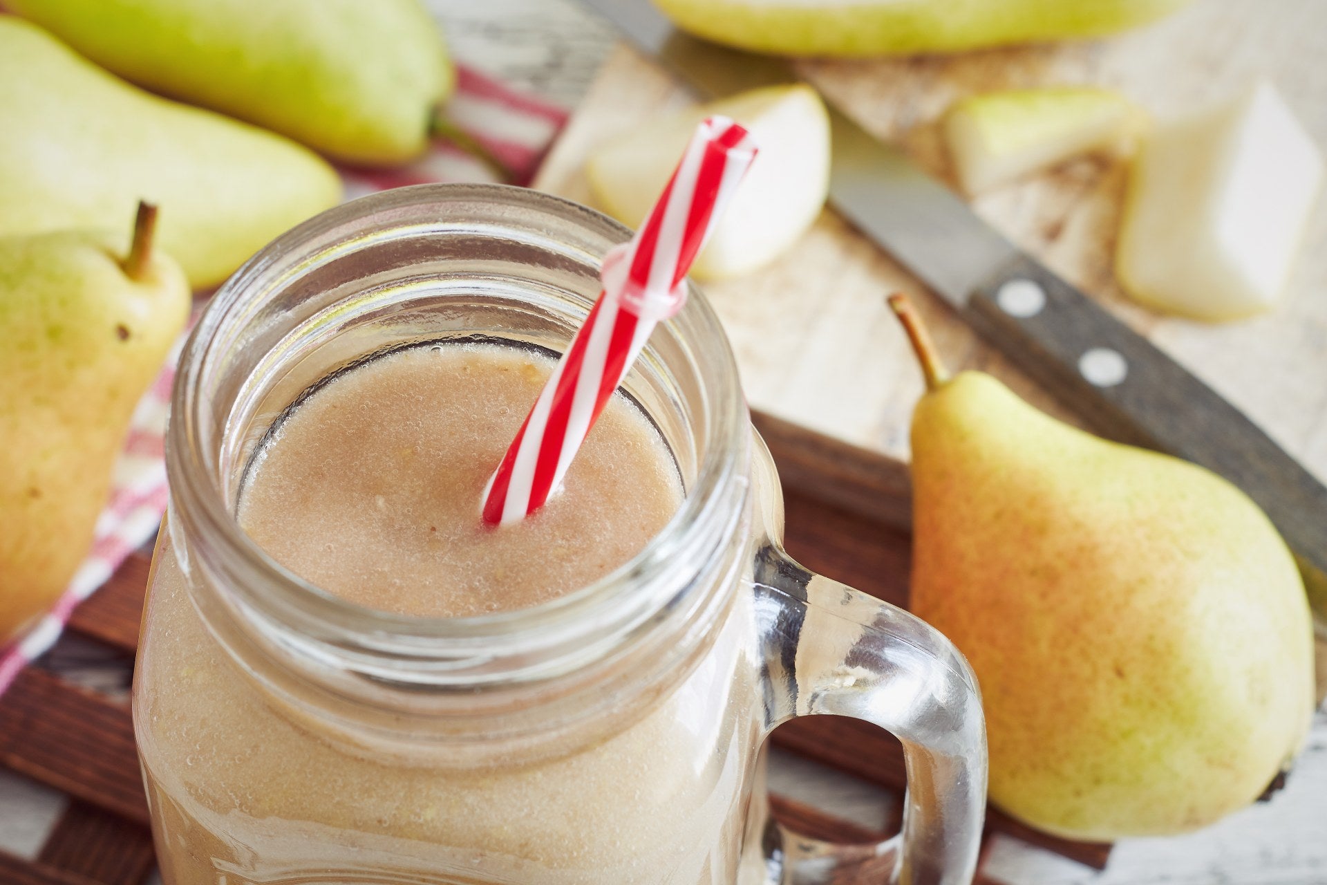 A glass mug with a pear smoothie and stripey straw