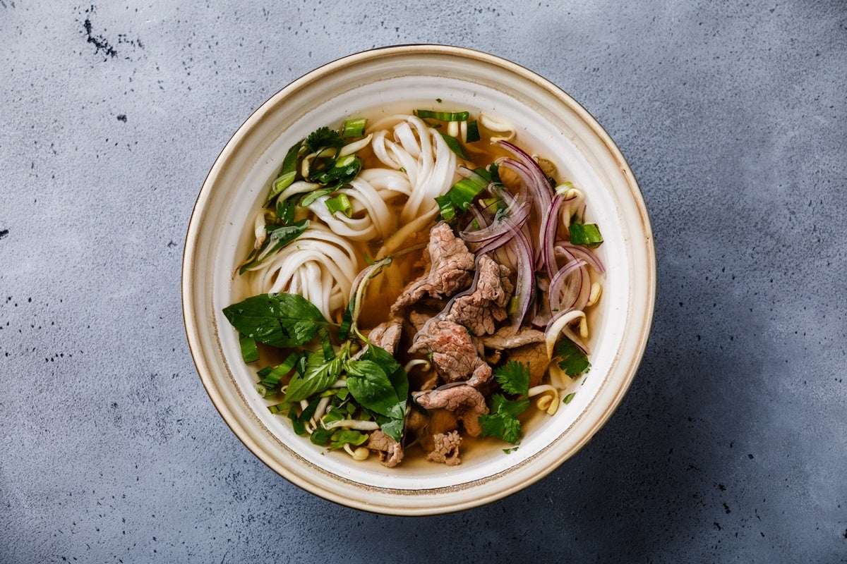 A steaming bowl of pho soup with noodles, herbs, and beef slices.