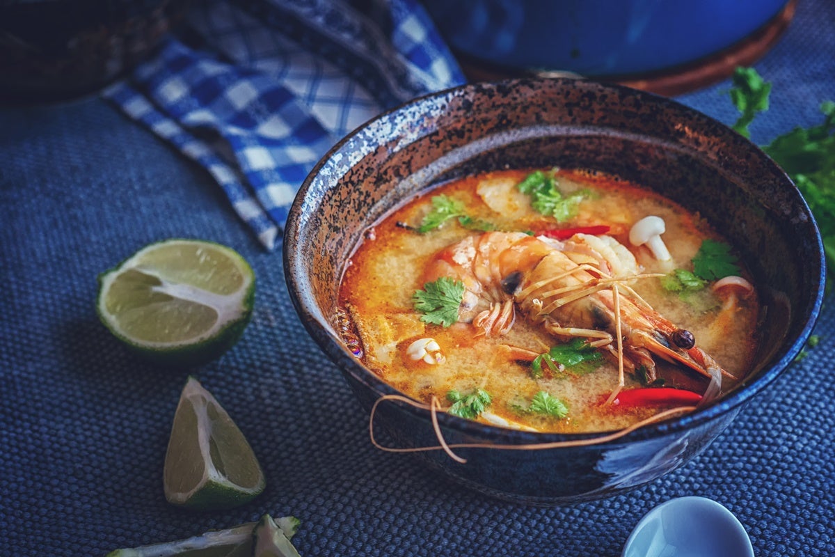 A fresh bowl of tom yam soup with fresh slices of lime set alongside