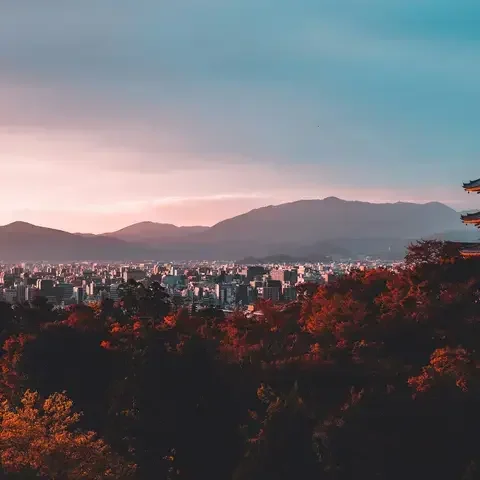 Kyoto cityscape at sunset with a traditional pagoda in the foreground and mountains in the distance