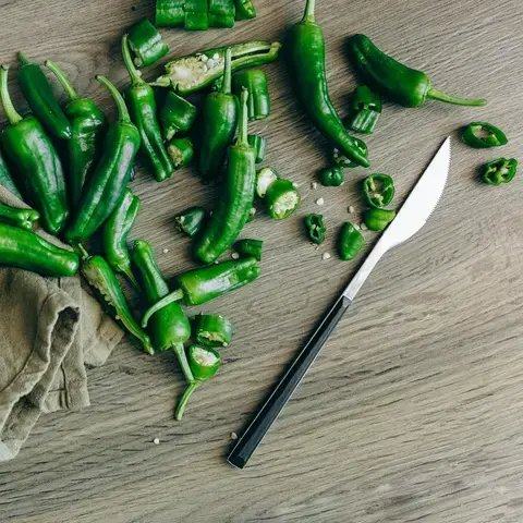 A chopping board and knife with green whole and sliced jalapeno peppers