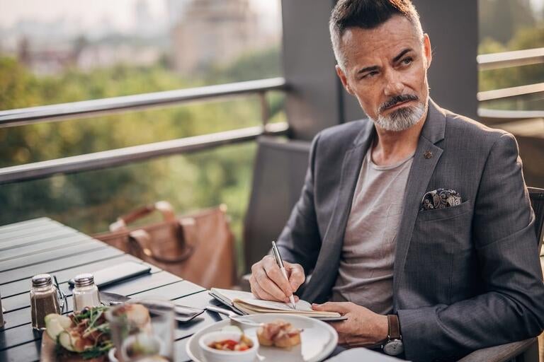 A man writing in a notebook at a restaurant table.