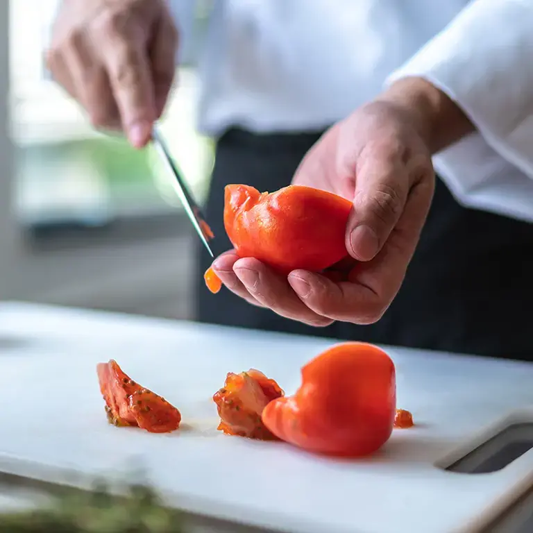 Tomatoes being halved on a chopping board.