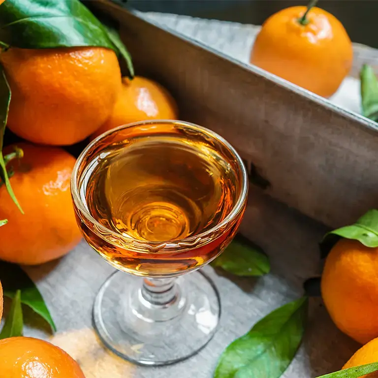 A glass of mandarino surrounded by oranges.
