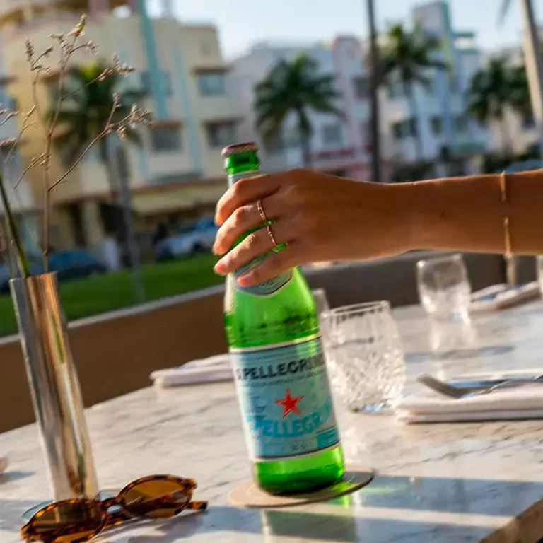 Hand holding a bottle of S.Pellegrino on a Miami restaurant terrace.