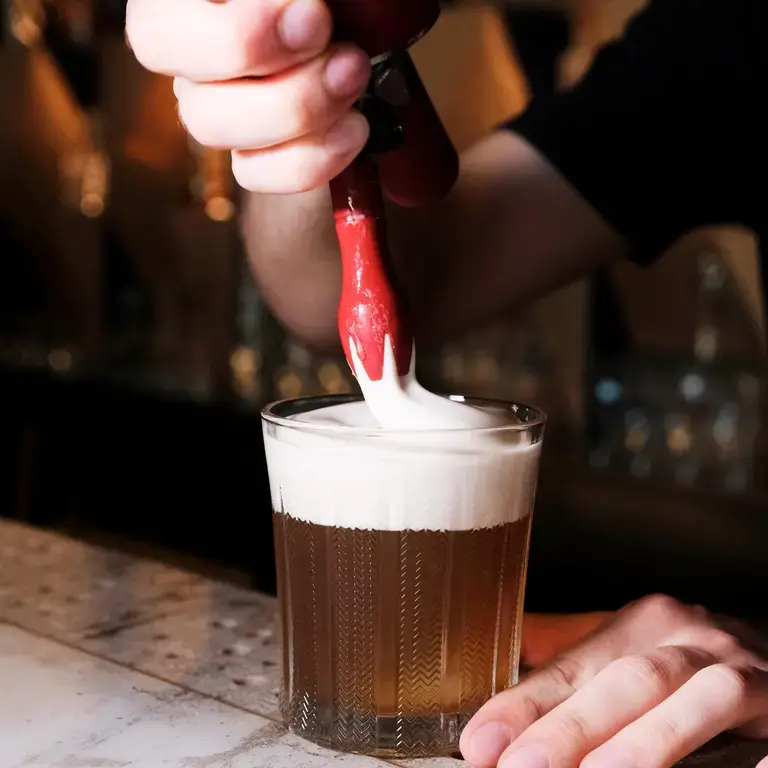 Adding foam with a siphon to a drink at Saint.