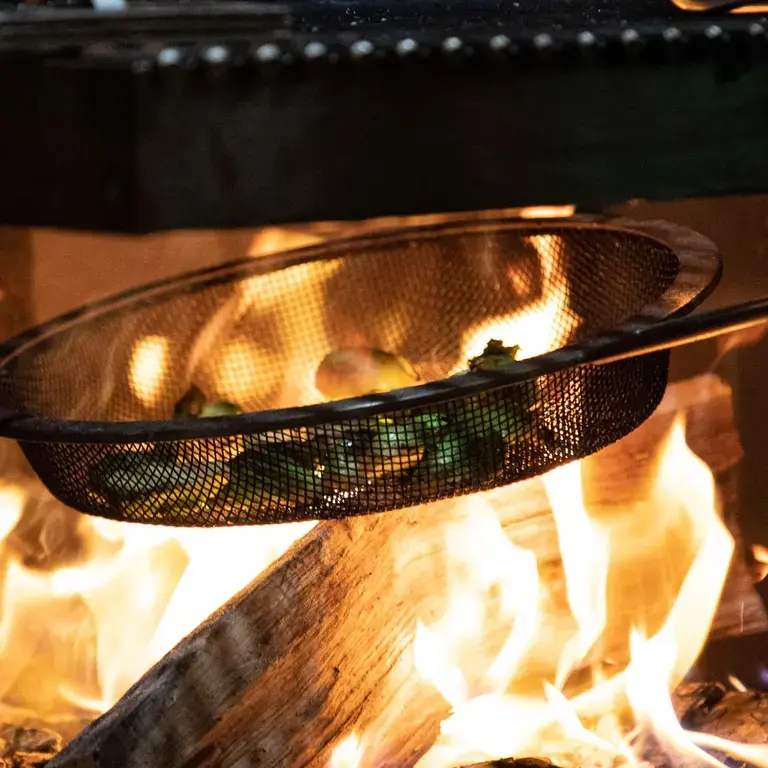 A grill pan above a fire with vegetables on in