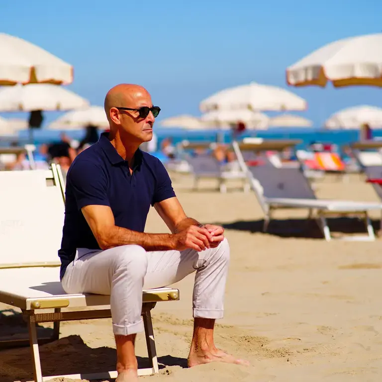 Stanley Tucci sat on a sun lounger on a sandy, sunny beach