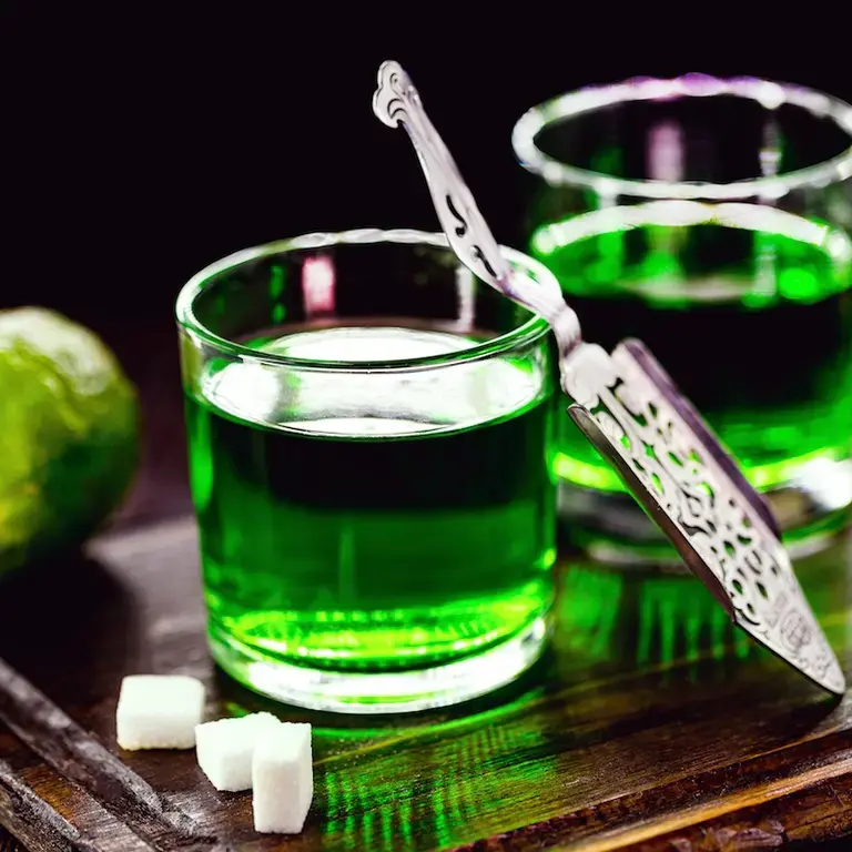 Two glasses of absinthe with sugar cubes and lime on the side.
