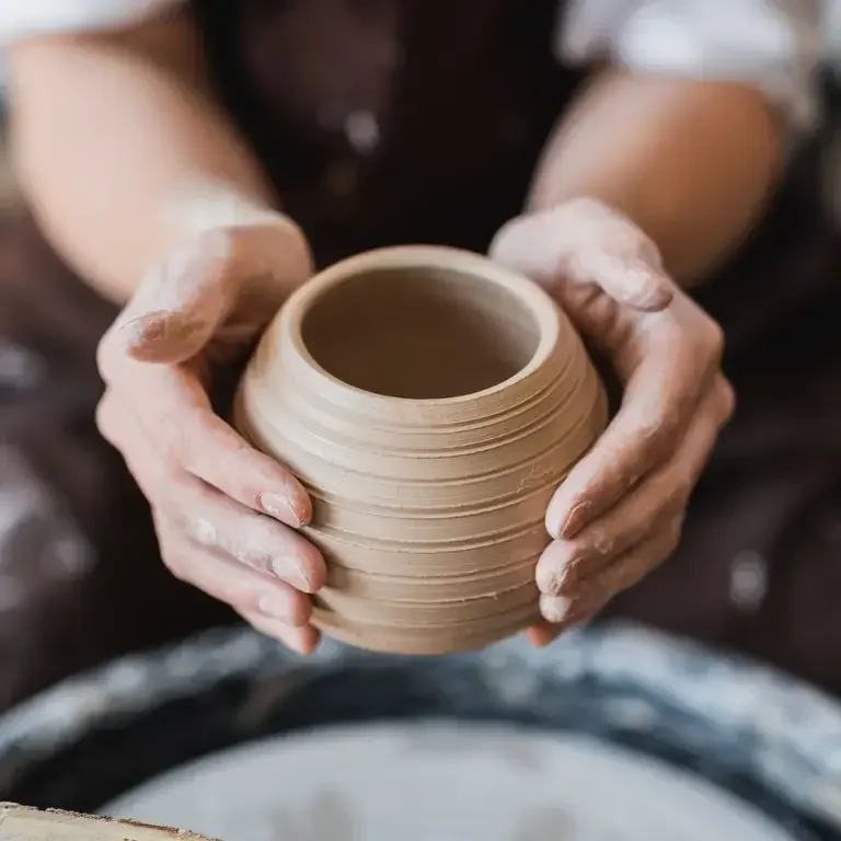 two hands lifring up a ceramic cup that's just made on a potter's wheel