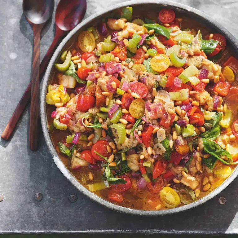 A bowl of caponata on a table with cutlery.