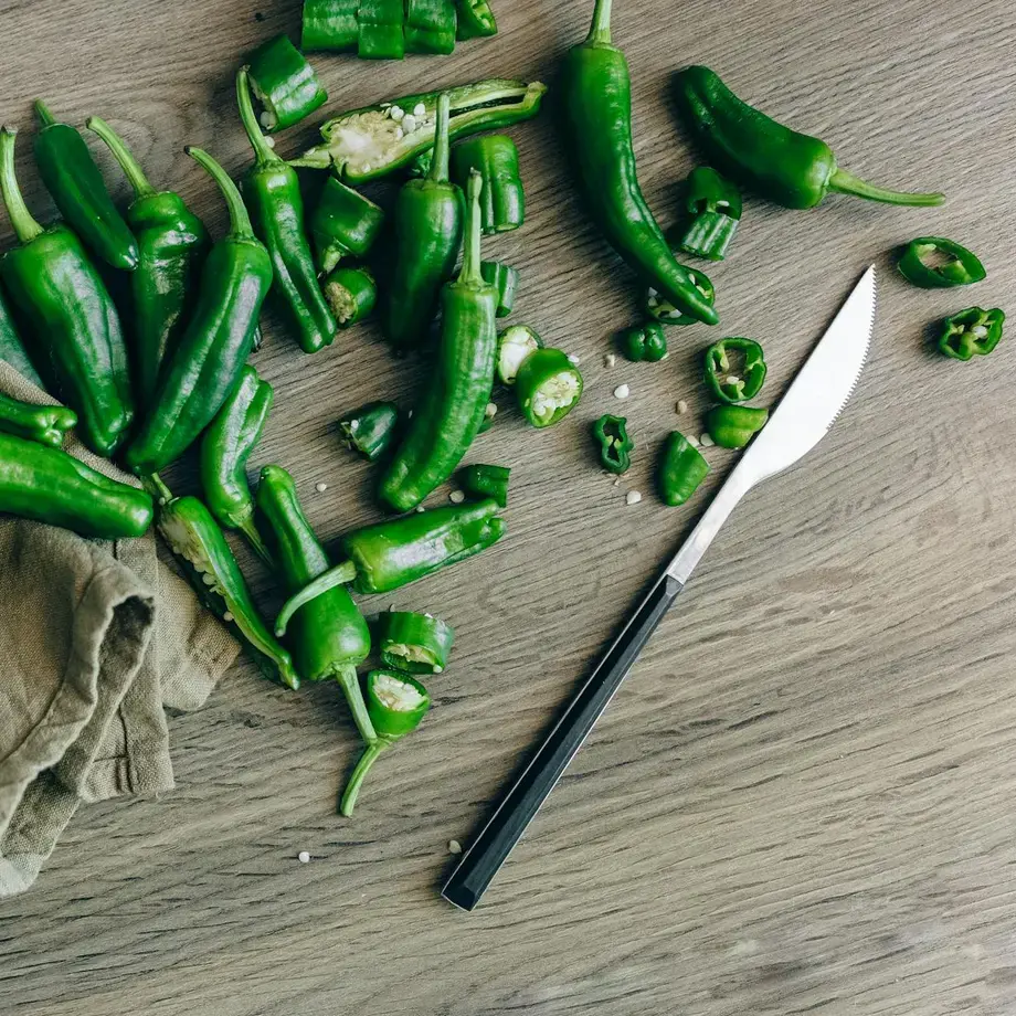 A chopping board and knife with green whole and sliced jalapeno peppers
