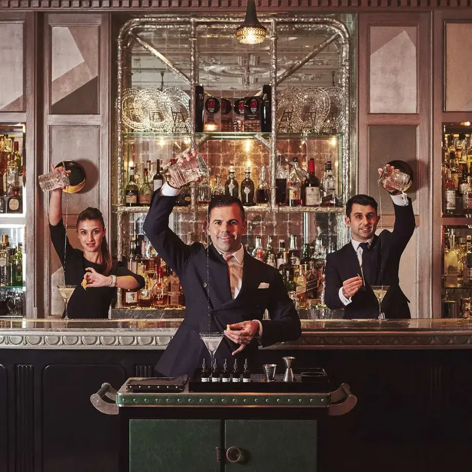 Three people mixing drinks at a bar.