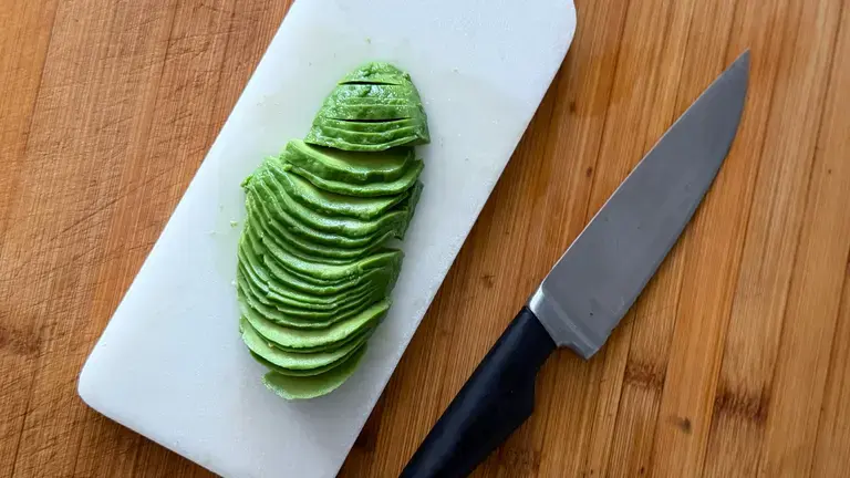 Sliced avocado on a chopping board, with a knife.