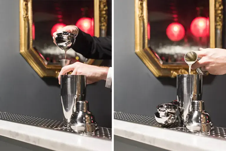 a hand squeezing a lemon with a manual juicer and dosing a jigger