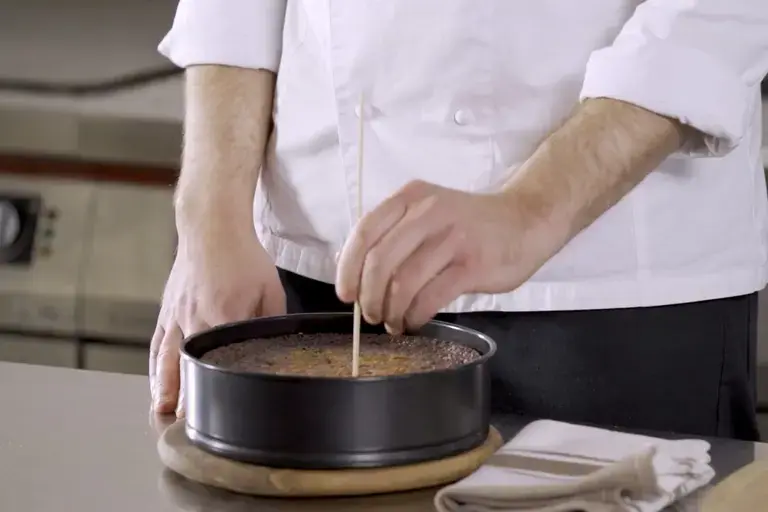 A chef puts a cake tester into a cake.