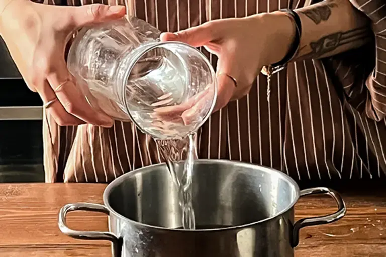 Chef pours water into a pot.