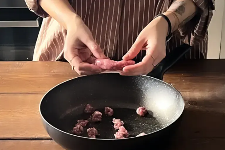 Chef breaks an Italian sausage in a pan.