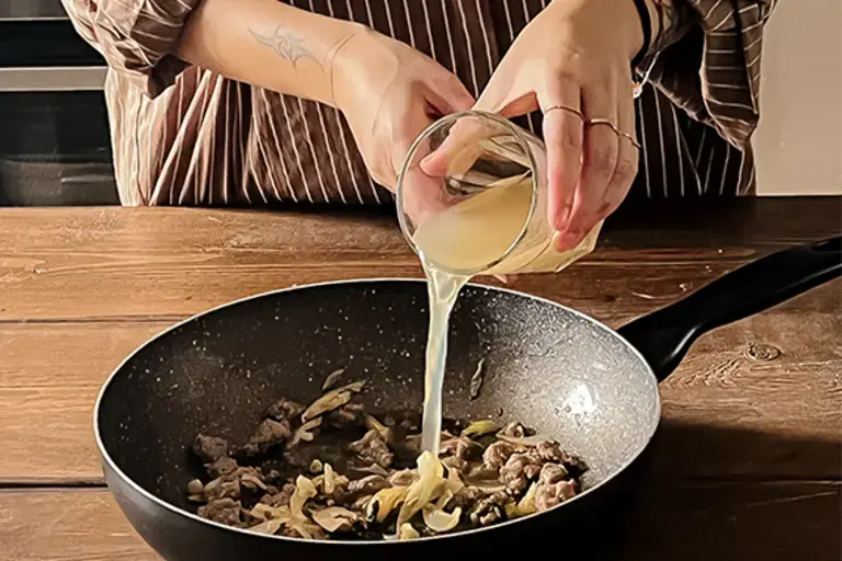 Chef pours vino bianco chicken stock into the pan.