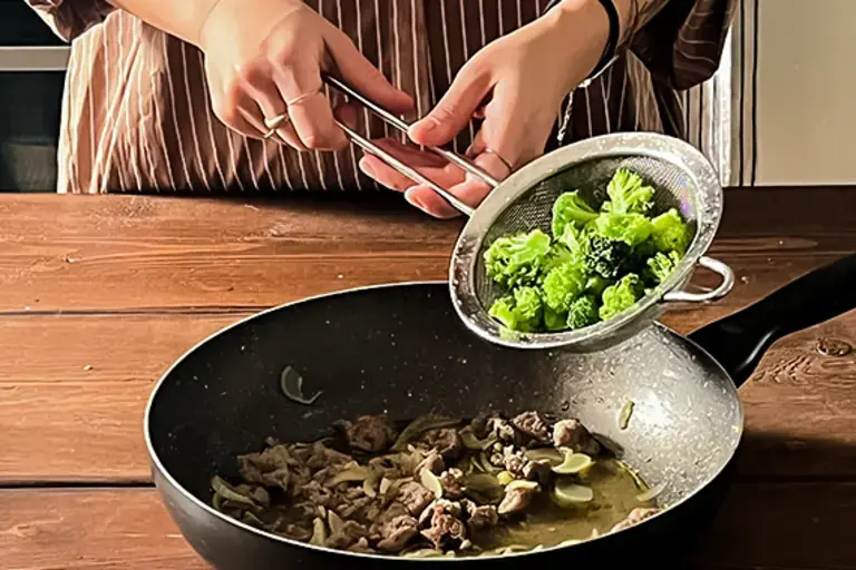 Chef adds broccolini to the pan.
