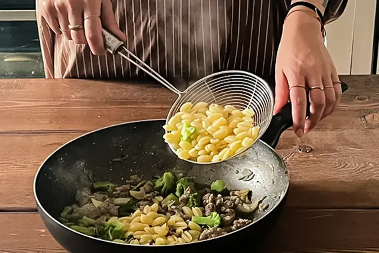 Chef adds pasta to the pan.