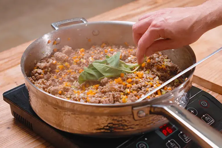 Adding herbs to the ragù.