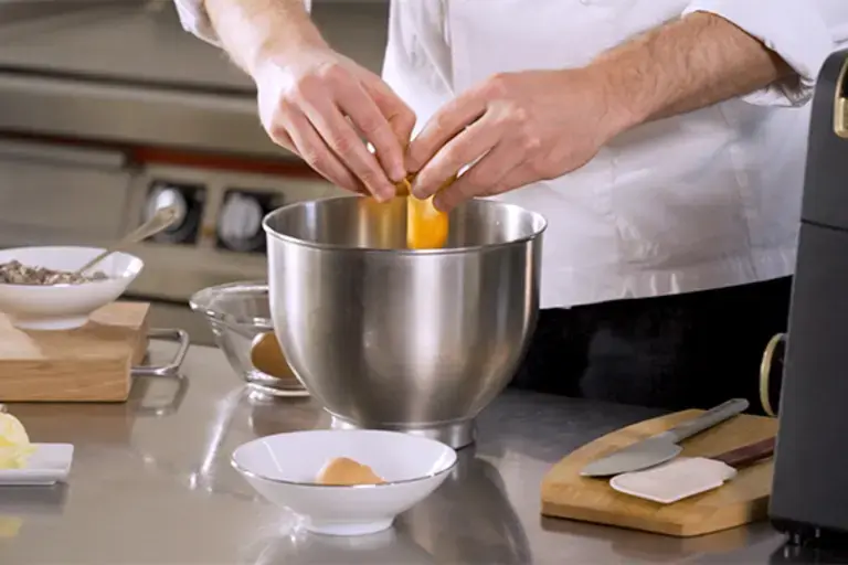 A chef cracks eggs into a bowl.