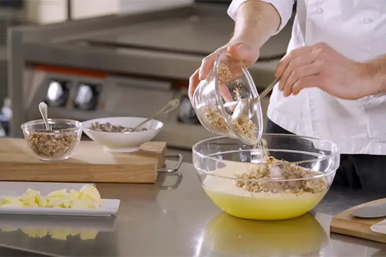 A chef pours breadcrumbs into a mixing bowl.