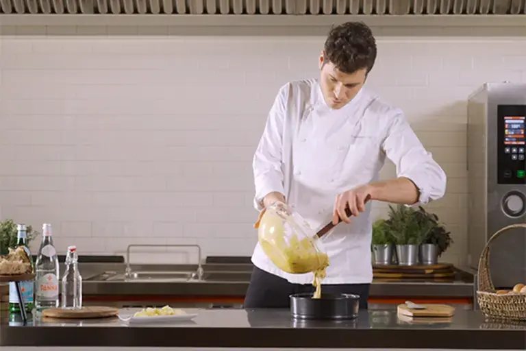 A chef pours cake mixture into a tin.