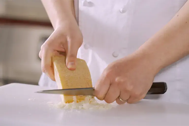 A rind of cheese being scraped with a knife.