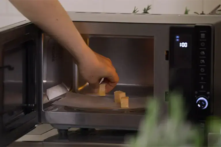 Chunks of cheese being placed into a microwave. 