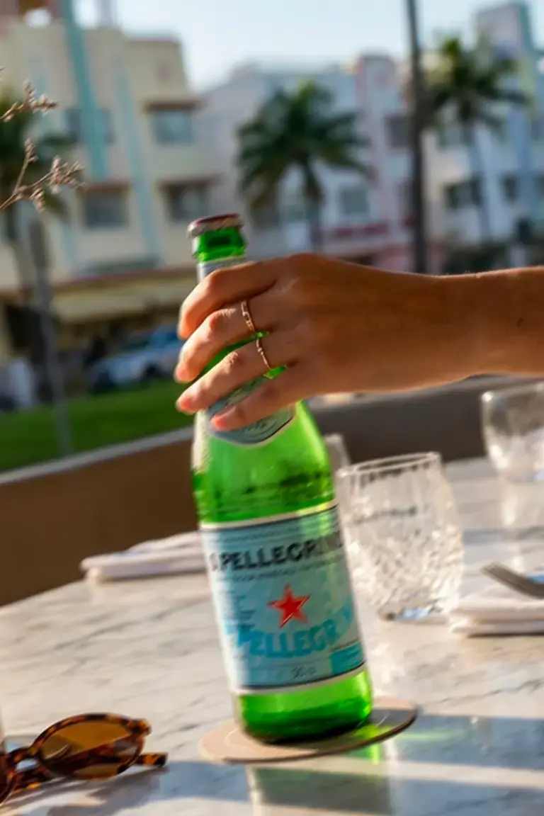 Hand holding a bottle of S.Pellegrino on a Miami restaurant terrace.