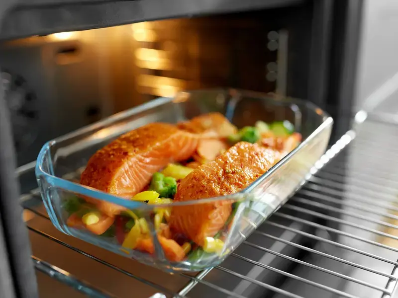 An ovenware dish containing two salmon fillets set on vegetables entering oven