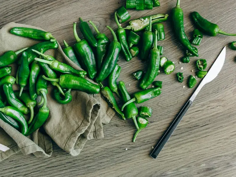 Chopping board and knife with green whole and sliced jalapenos.
